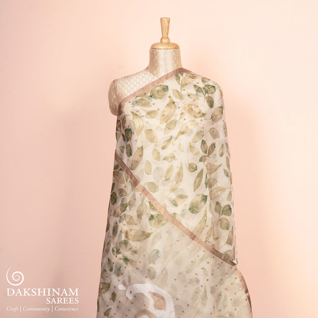 Saree with leaf pattern on a mannequin against a pink background, featuring the brand 'Dakshinam Sarees'.