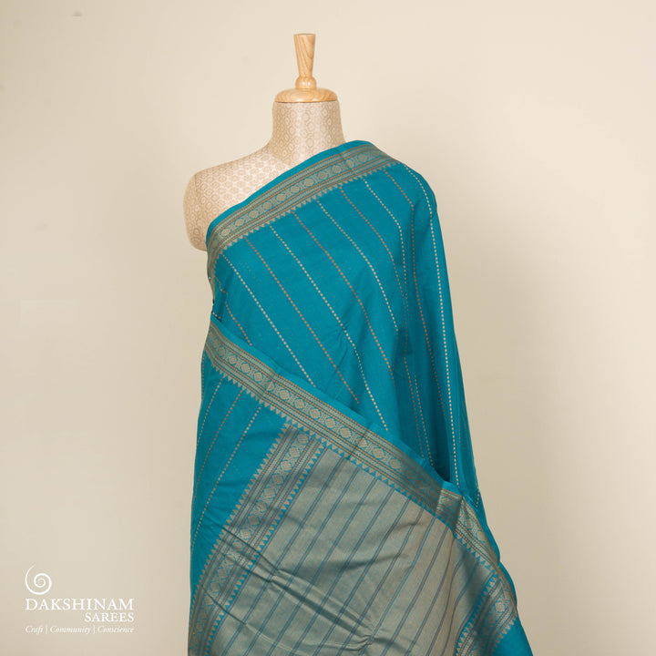Teal blue handloom Kanchi cotton saree with striped dash butta body, traditional temple and vairom butta border, matching teal blouse.