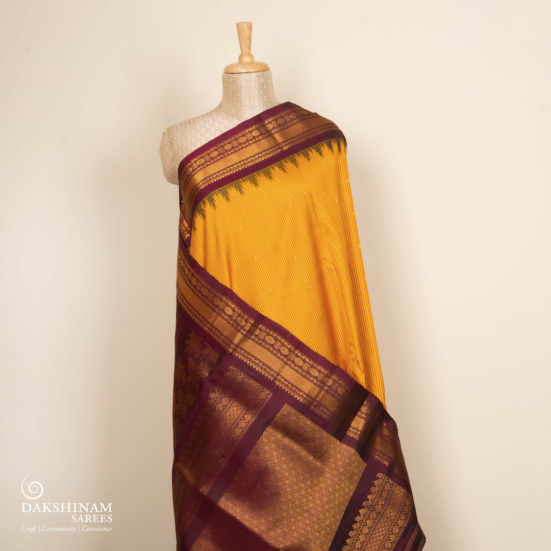 Yellow Gadwal silk saree with maroon checks and small butta body, maroon zari border with chakram and temple motifs, plain maroon blouse.