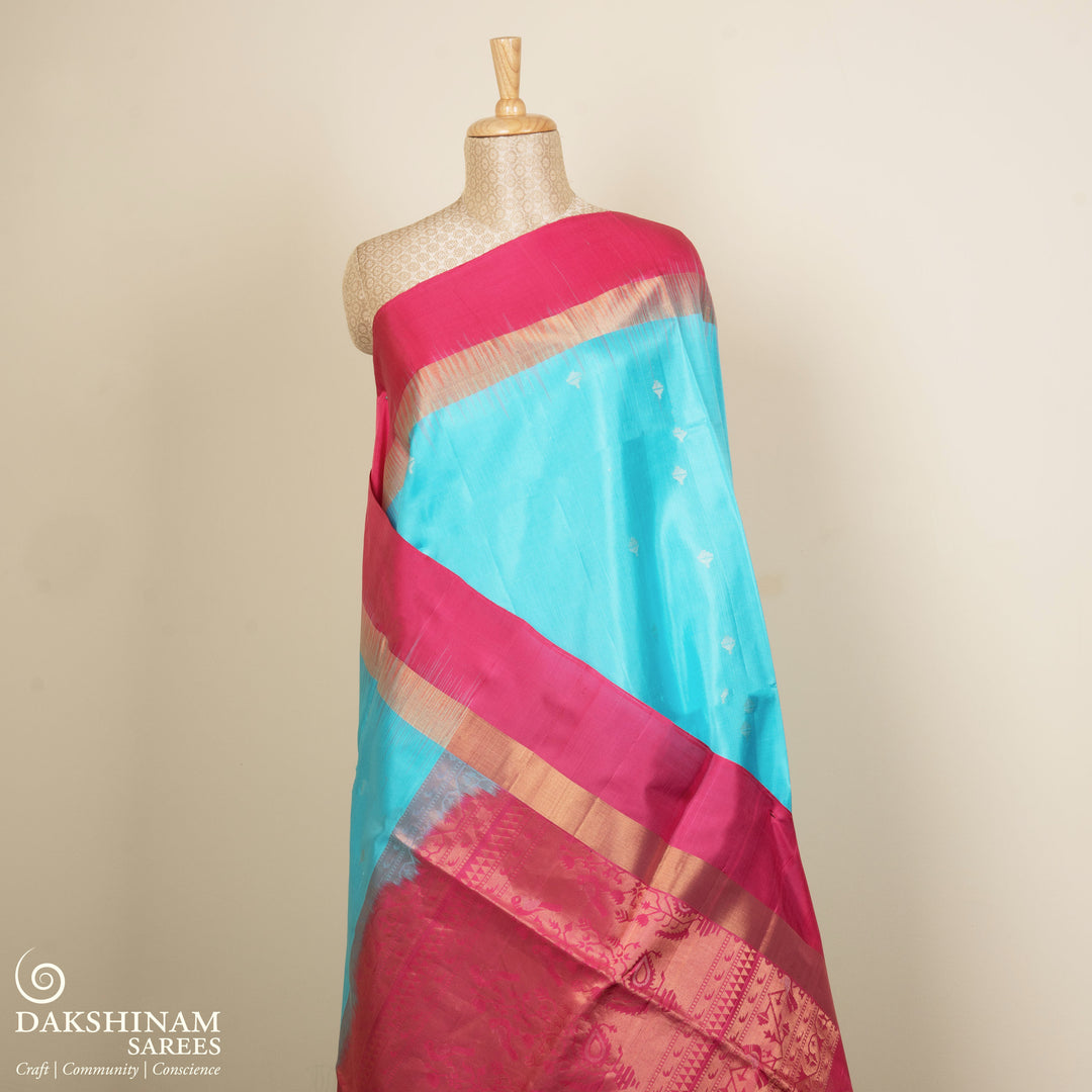 Light blue soft silk saree with silver butta allover, pink and gold zari border and pink pallu with bird and plant motifs.