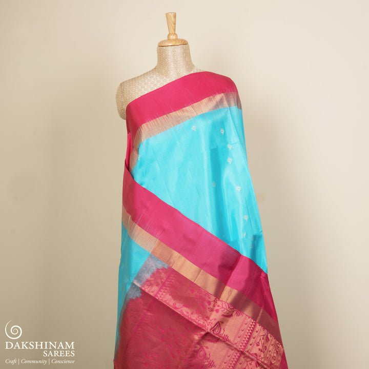 Light blue soft silk saree with silver butta allover, pink and gold zari border and pink pallu with bird and plant motifs.