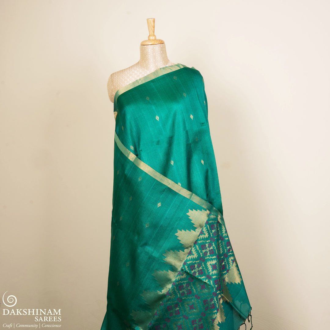 Green Tussar soft silk saree with floral butta body, gold border and pallu with temple design and purple buttas, paired with plain green blouse.