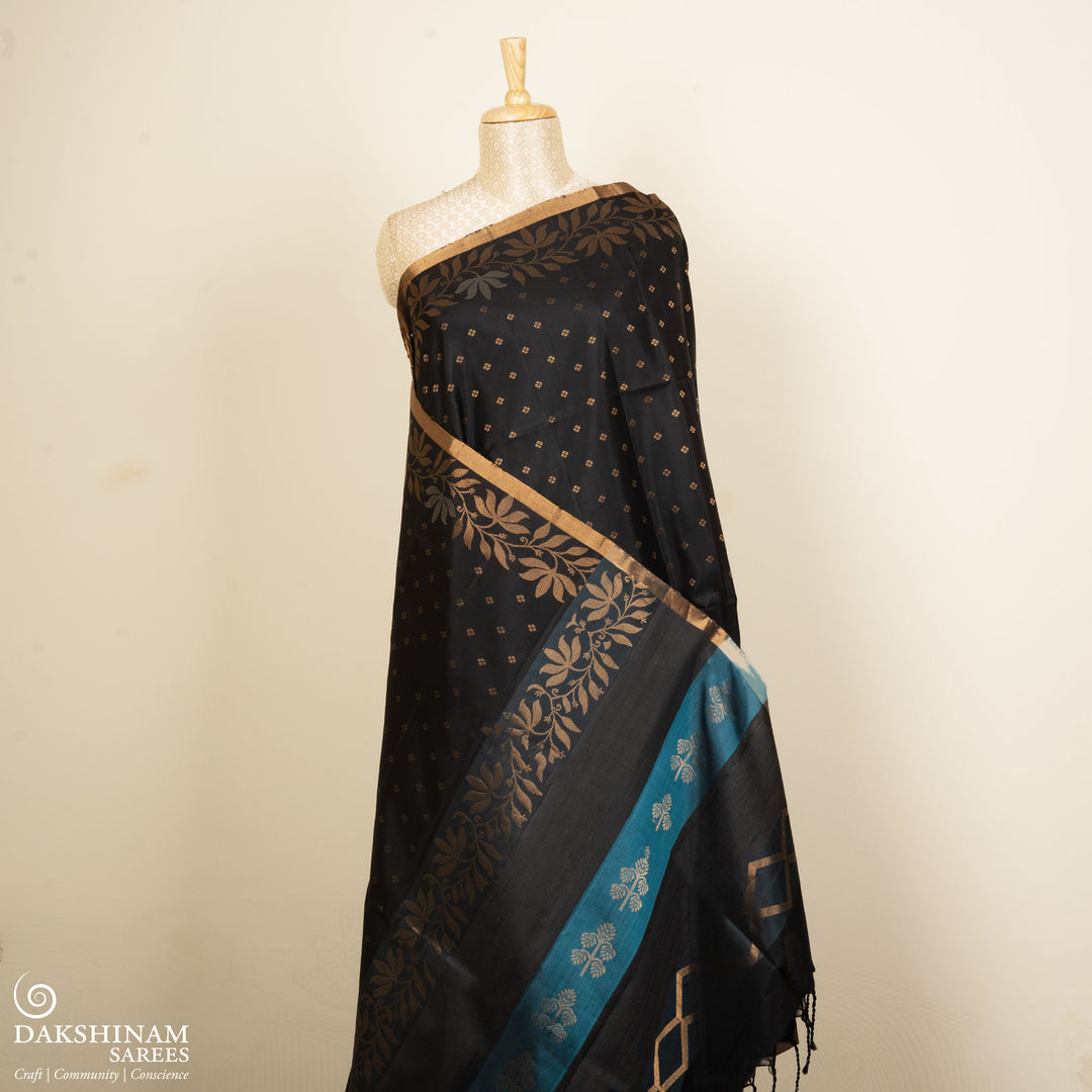 Black soft silk saree with small gold and silver zari buttas, floral border and blue contrast pallu with diamond and floral motifs.