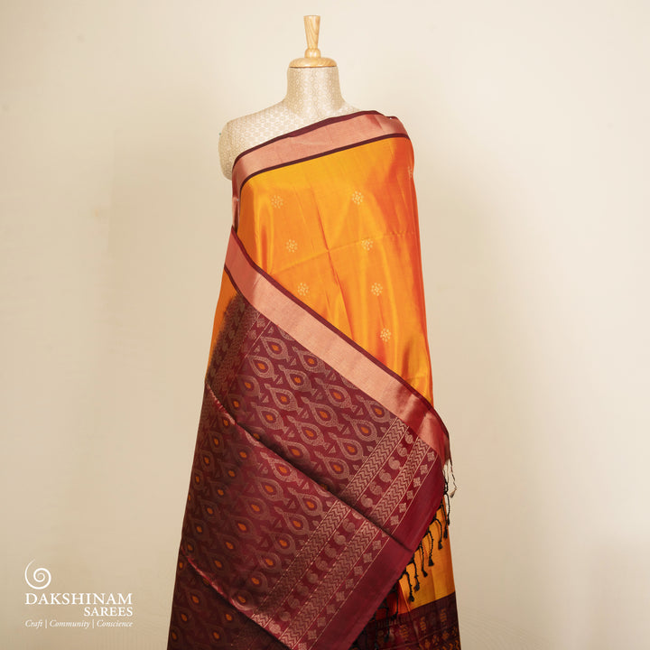 Orange soft silk saree with floral butta body, maroon border with paisley and chevron motifs, and maroon pallu with diamond floral patterns.