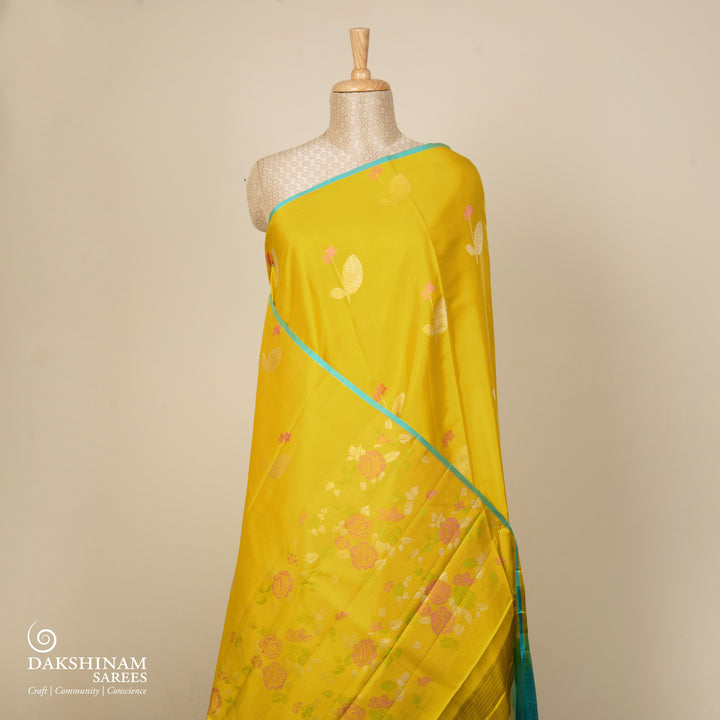 Lime green handwoven Kanjivaram silk saree with floral and leaf motifs, rose design pallu, borderless style, paired with light blue blouse with silver zari stripes.