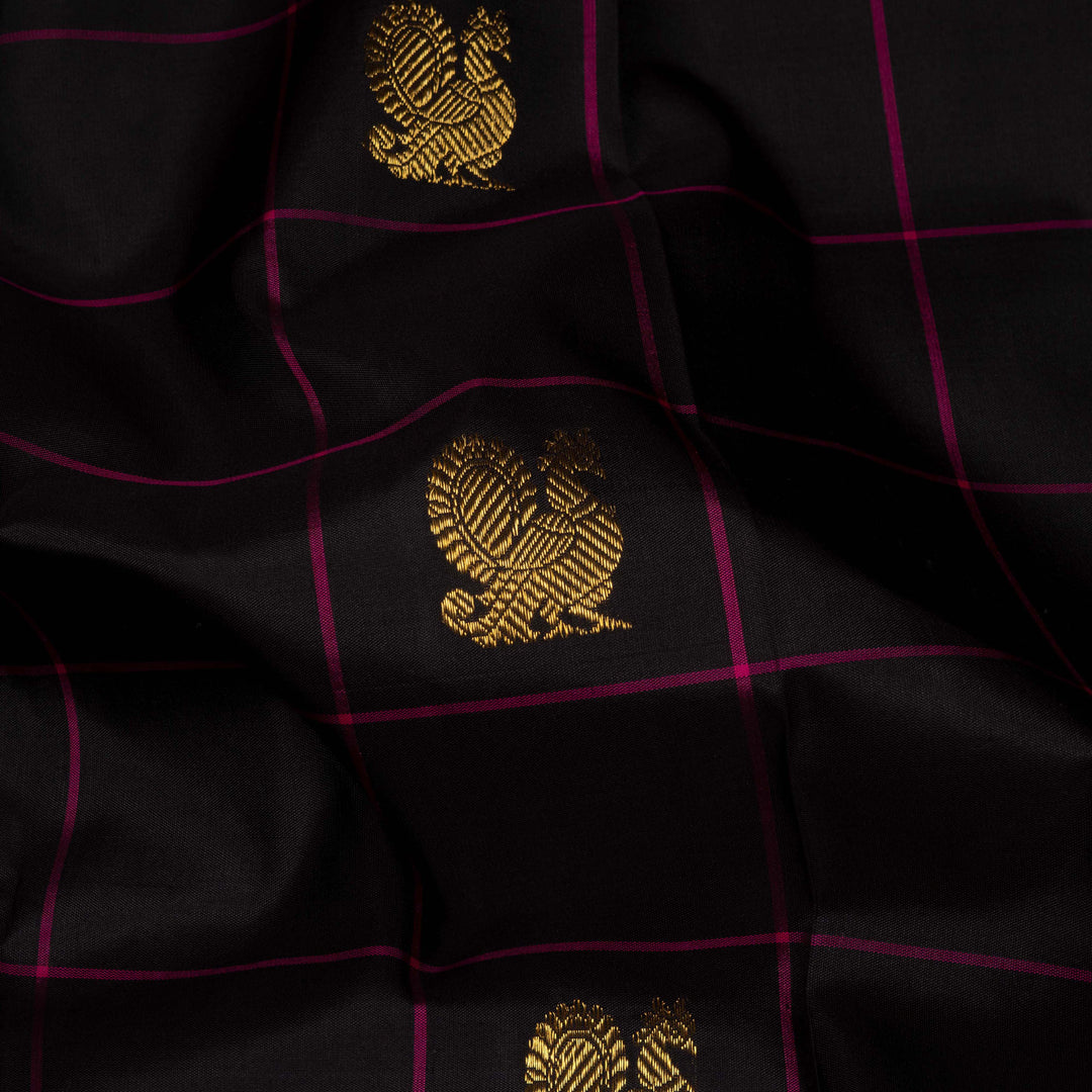 Black handwoven Kanjivaram silk saree with magenta checks, annam and chakram motifs, and pink pallu with gold zari chevron and leaf designs, paired with magenta blouse.