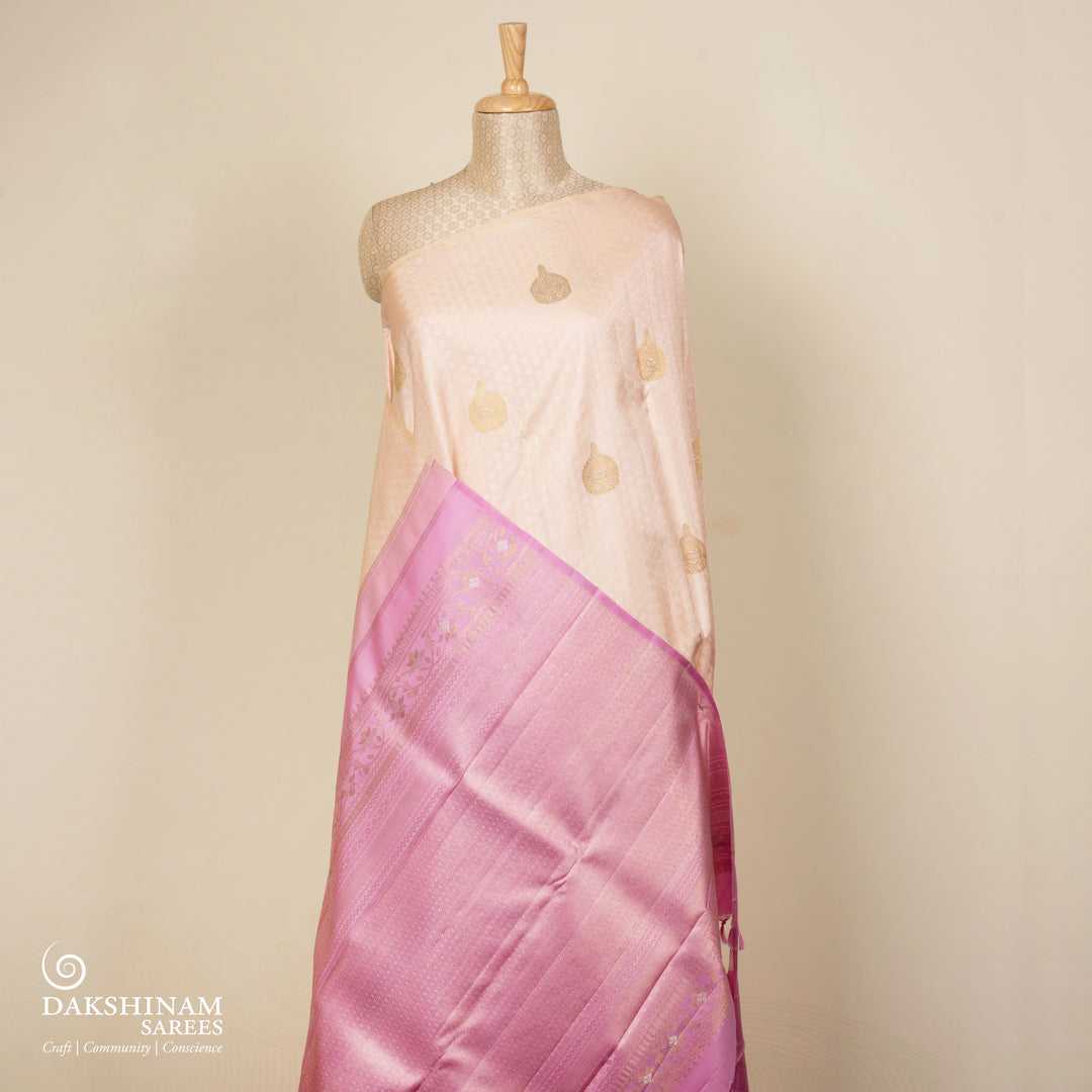 Beige handwoven Kanjivaram silk saree with self design and gold zari floral motifs, lavender border and pallu with chevron and floral patterns, paired with lavender blouse.