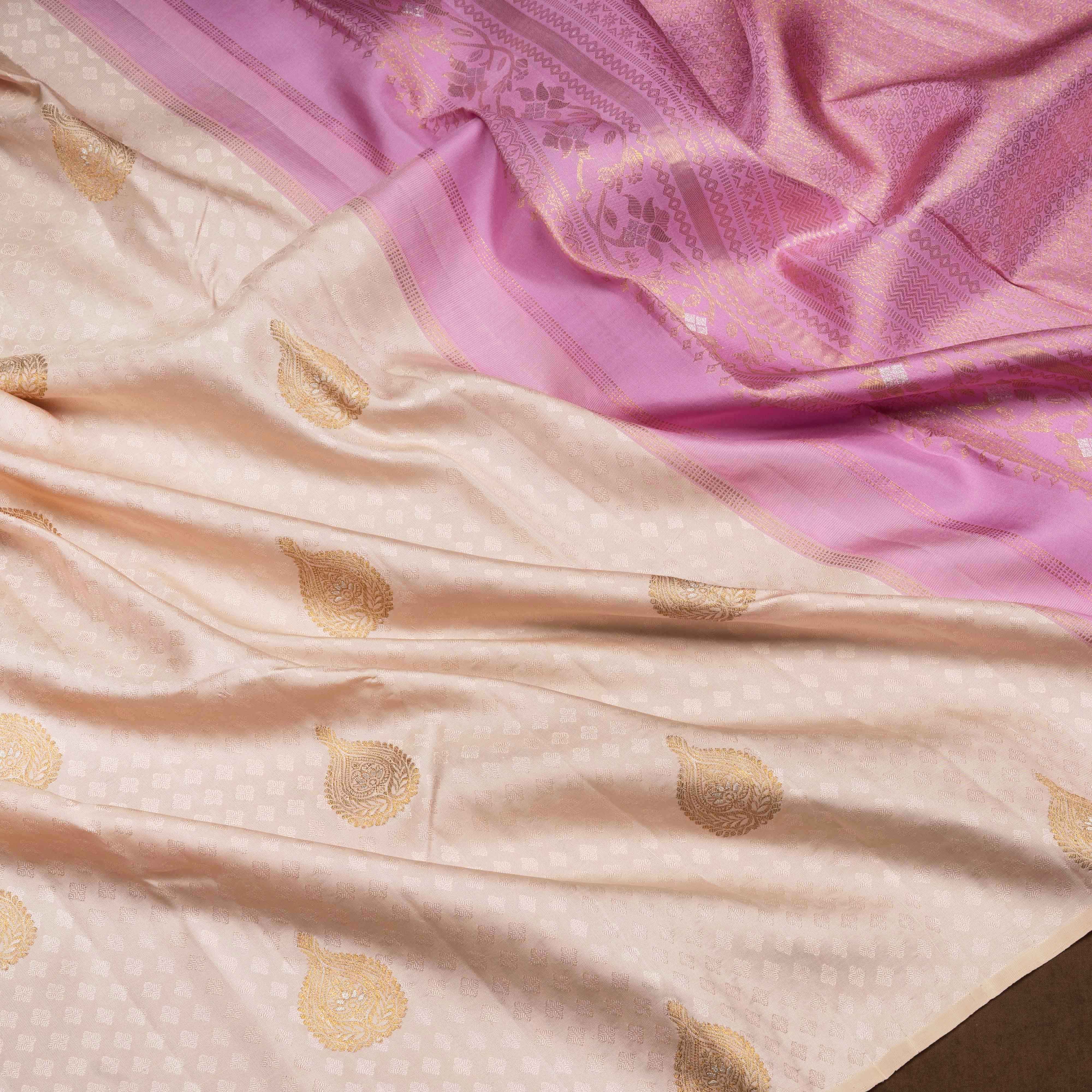 Beige handwoven Kanjivaram silk saree with self design and gold zari floral motifs, lavender border and pallu with chevron and floral patterns, paired with lavender blouse.
