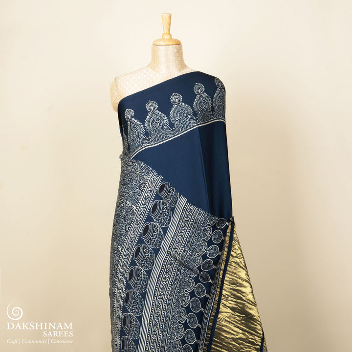 Blue handwoven modal silk cotton saree with plain blue body, Ajrakh printed border, gold zari pallu, paired with a blue Ajrakh design blouse.