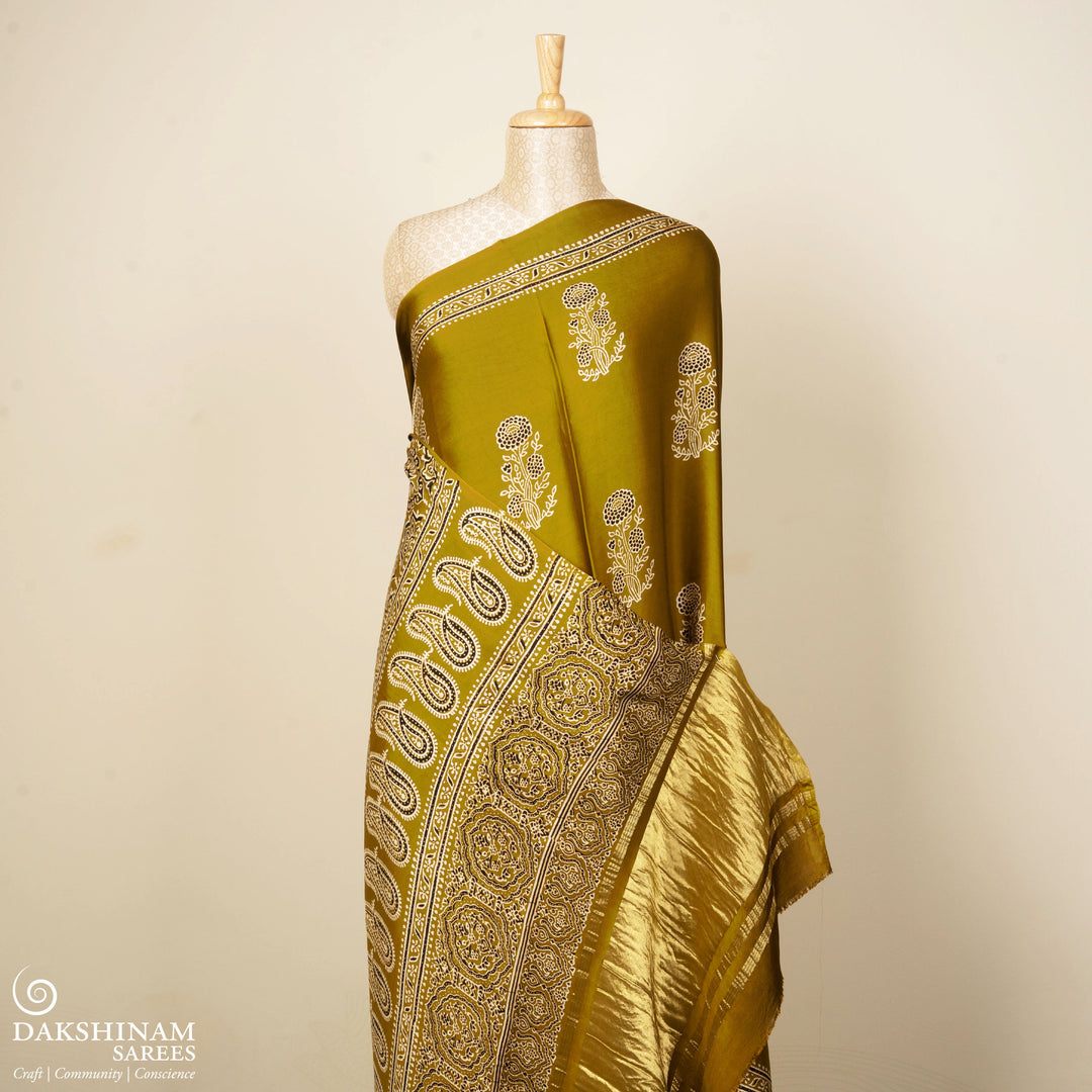 Mustard handwoven modal silk saree with floral motifs on body, Ajrakh printed border, gold zari pallu, paired with a mustard Ajrakh design blouse.