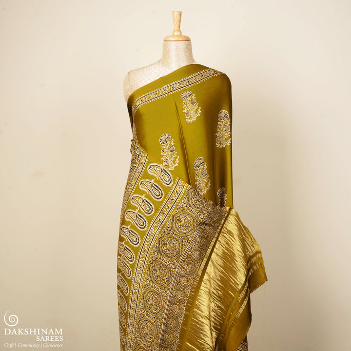 Mustard handwoven modal silk saree with floral motifs on body, Ajrakh printed border, gold zari pallu, paired with a mustard Ajrakh design blouse.