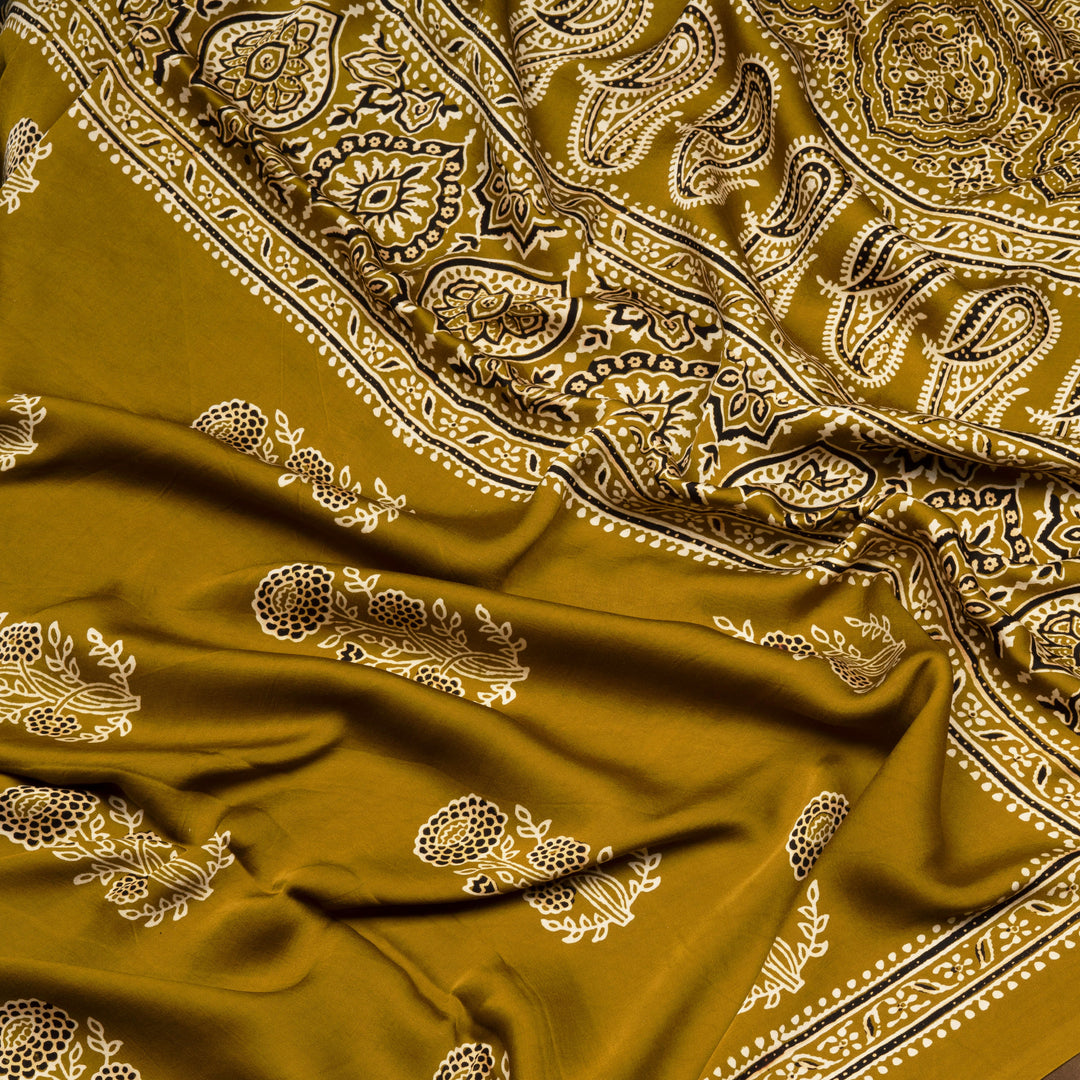 Mustard handwoven modal silk saree with floral motifs on body, Ajrakh printed border, gold zari pallu, paired with a mustard Ajrakh design blouse.