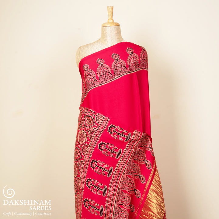 Pink handwoven modal silk saree with plain pink body, Ajrakh printed border, gold zari pallu, paired with a pink Ajrakh design blouse.