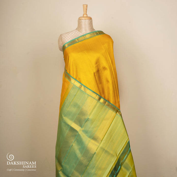 Yellow Kanjivaram silk saree with plain body, aqua blue dual-tone getti border and blue green paneled pallu with matching blouse