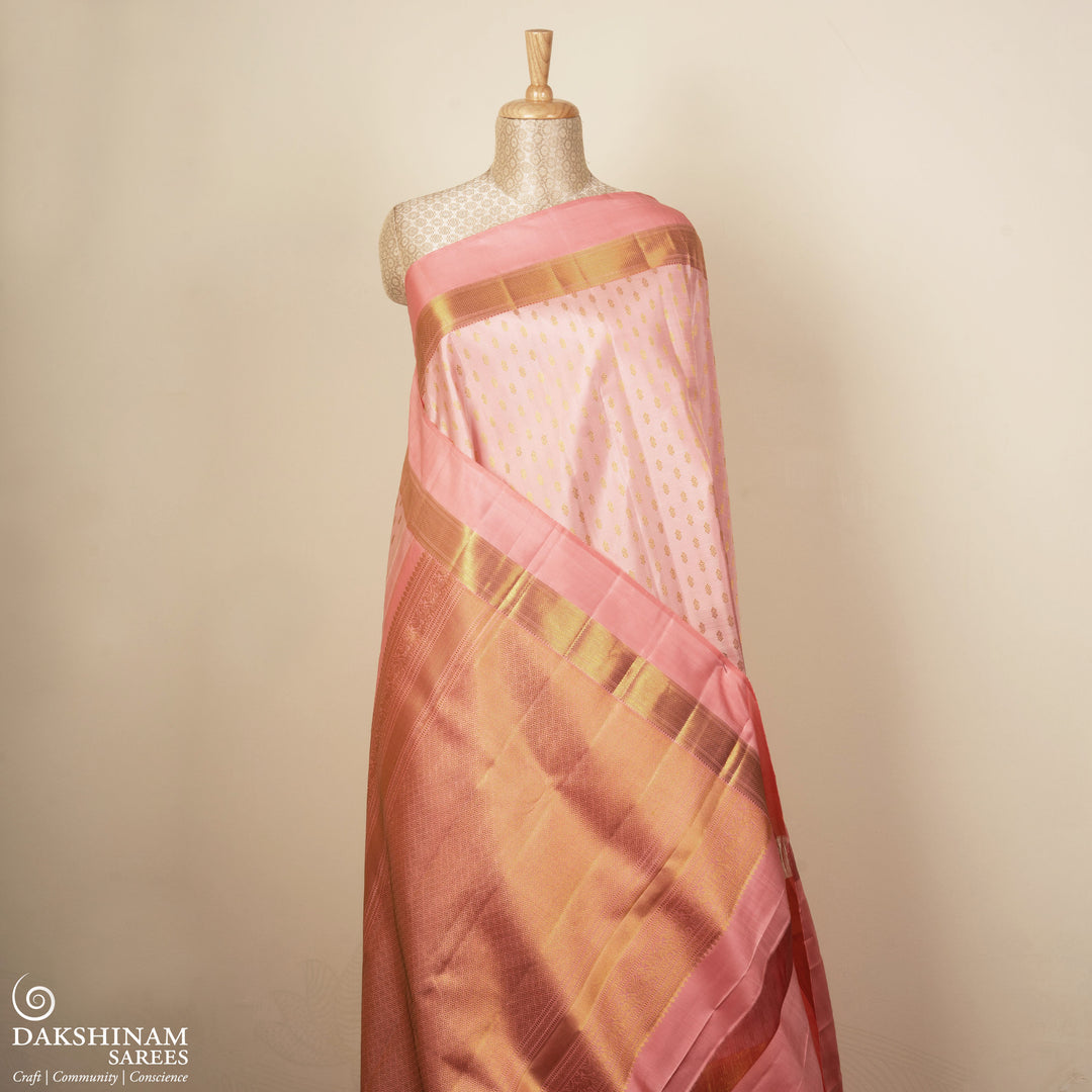 Light peach Kanjivaram silk saree with vairam buttas, peach pink border featuring temple and chevron designs, and detailed zari pallu, paired with plain blouse.