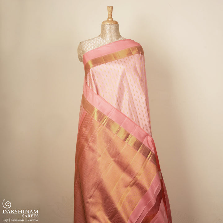 Light peach Kanjivaram silk saree with vairam buttas, peach pink border featuring temple and chevron designs, and detailed zari pallu, paired with plain blouse.