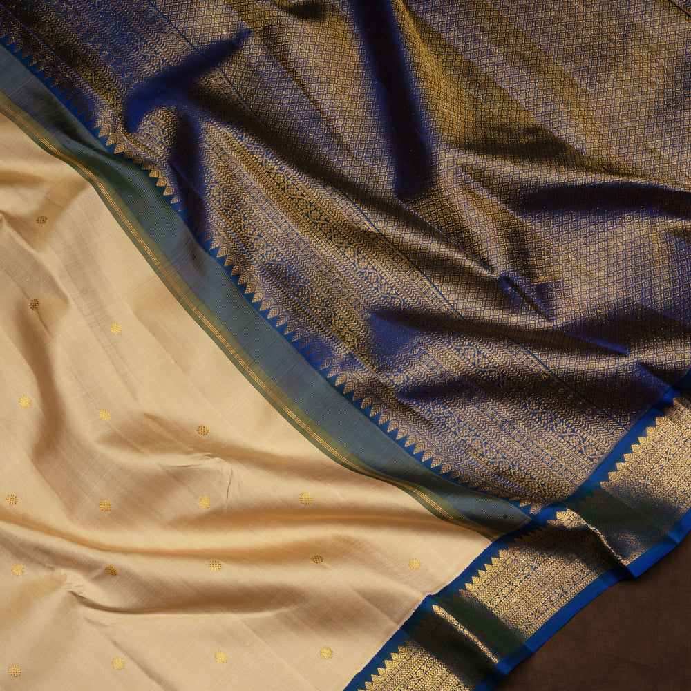Cream Kanjivaram silk saree with chakram buttas, peacock blue border featuring chevron, rudraksham and floral lines, paired with plain blue blouse.