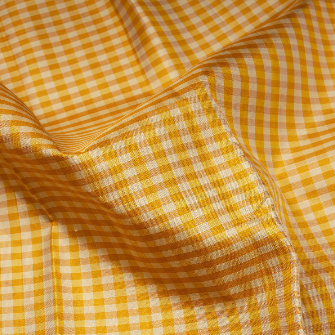 Beige and yellow small checked Kanjivaram silk saree with purple pallu featuring floral motifs, chevron and chakram designs, paired with dotted butta blouse.