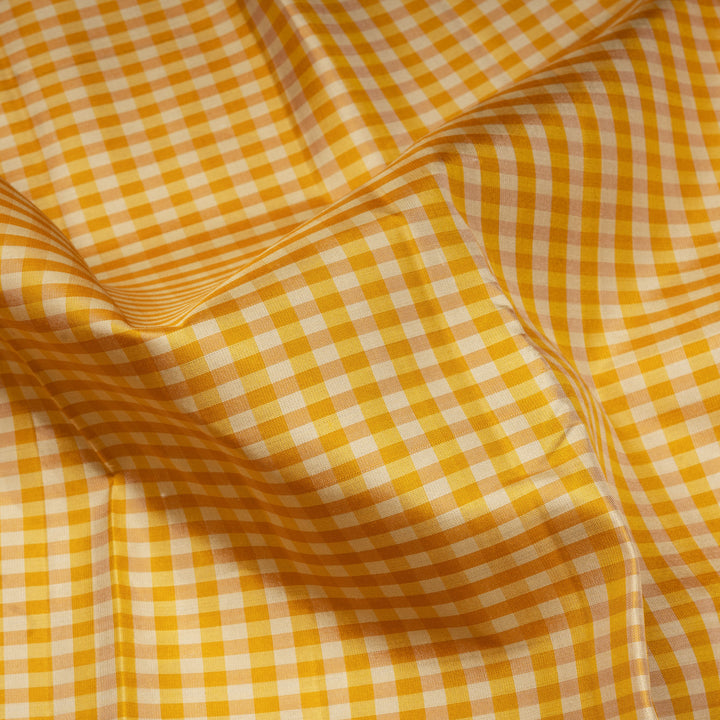 Beige and yellow small checked Kanjivaram silk saree with purple pallu featuring floral motifs, chevron and chakram designs, paired with dotted butta blouse.