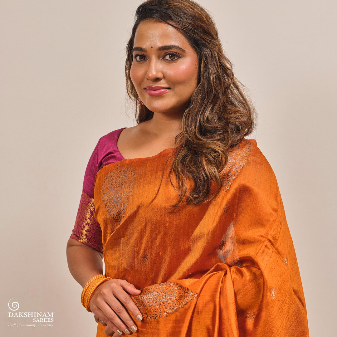 Woman wearing an orange saree with a purple blouse against a beige background