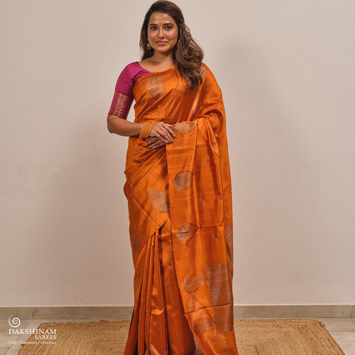 Woman wearing an orange saree with a pink blouse against a plain background