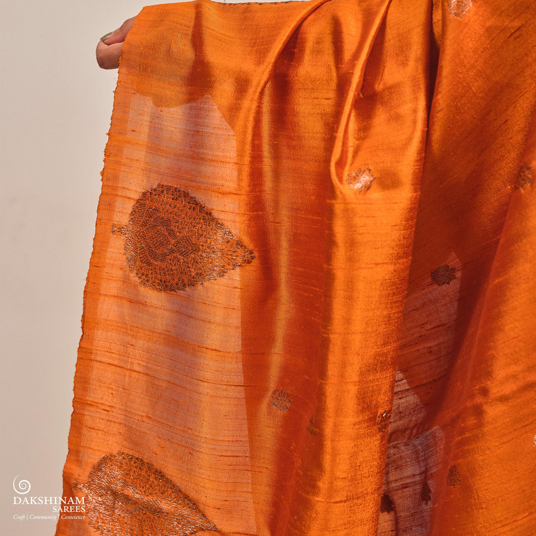 Orange fabric with intricate patterns held by a hand against a beige background