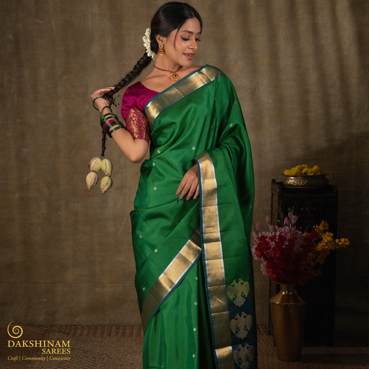 Green soft silk saree with small all-over buttas, peacock green border featuring gold zari Bavanchi designs and silver zari chevron edges, Rettaberunda motif pallu and matching blouse.