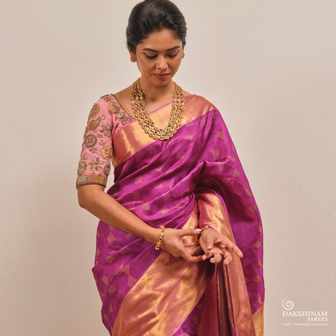 Woman wearing a traditional pink and gold saree with jewelry on a plain background