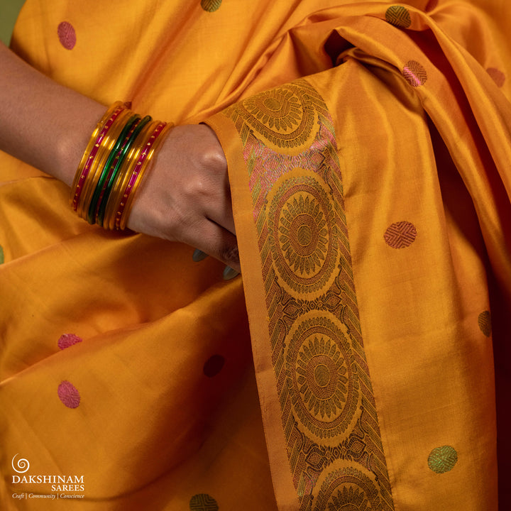 Yellow Kanjivaram silk saree with multicolor zari, red and green rudraksham buttas, green and red chakram border, floral pallu and plain yellow blouse with running border.