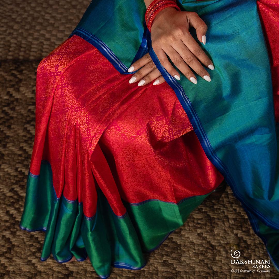 Orange no-zari Kanjivaram silk saree with light orange thread detailing, peacock green long border with silver zari lines, peacock blue pallu and matching blue blouse.
