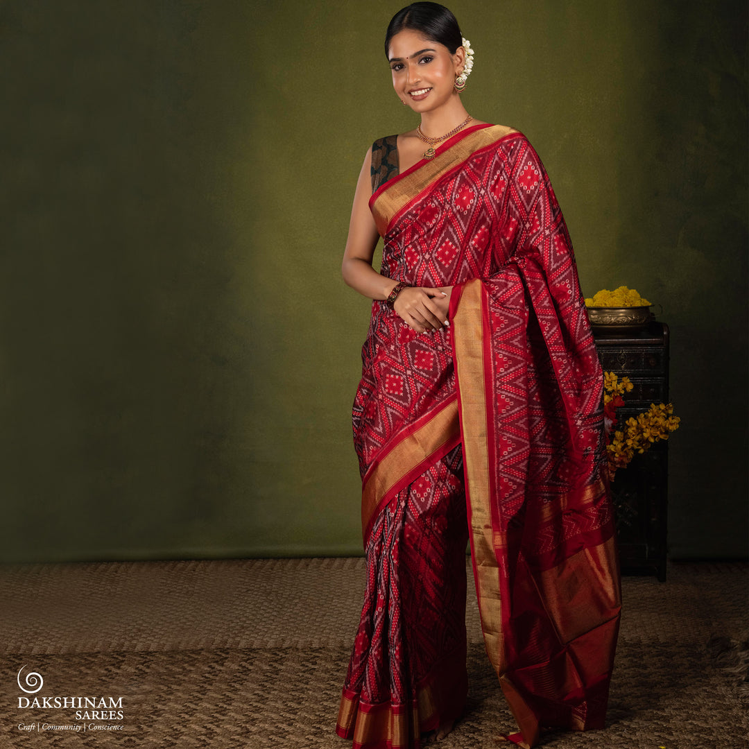Red Ikat saree featuring maroon and grey diamond-shaped designs, gold zari border, chevron panel pallu with temple design, paired with a plain red blouse.