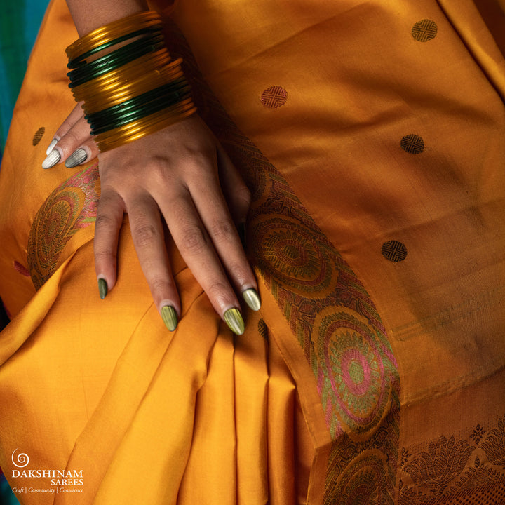 Yellow Kanjivaram silk saree with multicolor zari, red and green rudraksham buttas, green and red chakram border, floral pallu and plain yellow blouse with running border.