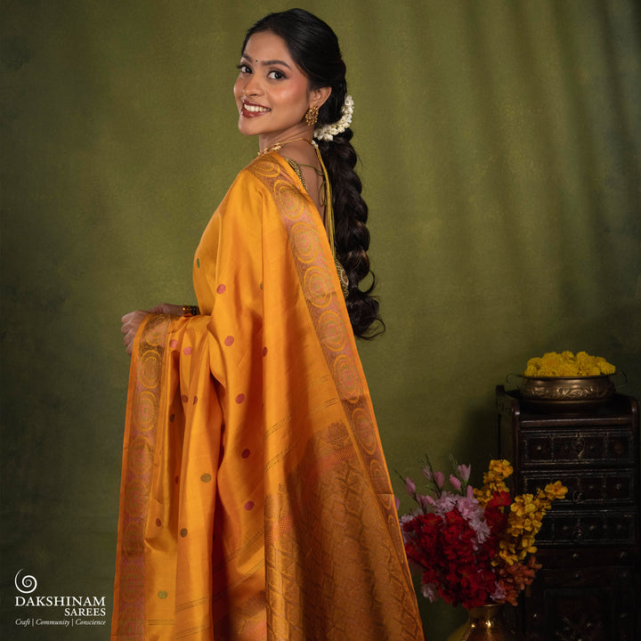 Yellow Kanjivaram silk saree with multicolor zari, red and green rudraksham buttas, green and red chakram border, floral pallu and plain yellow blouse with running border.