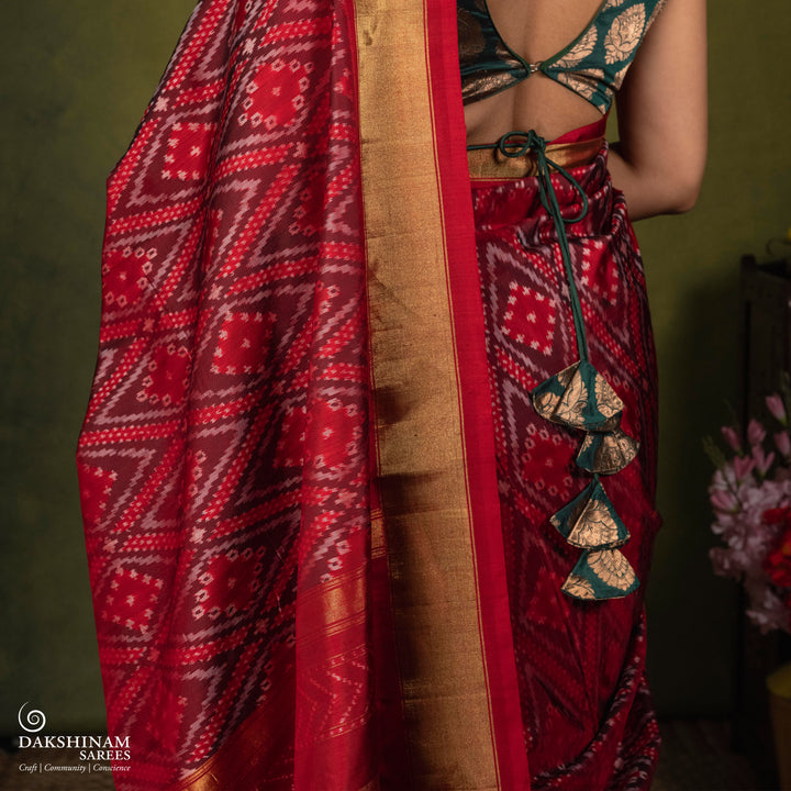 Red Ikat saree featuring maroon and grey diamond-shaped designs, gold zari border, chevron panel pallu with temple design, paired with a plain red blouse.